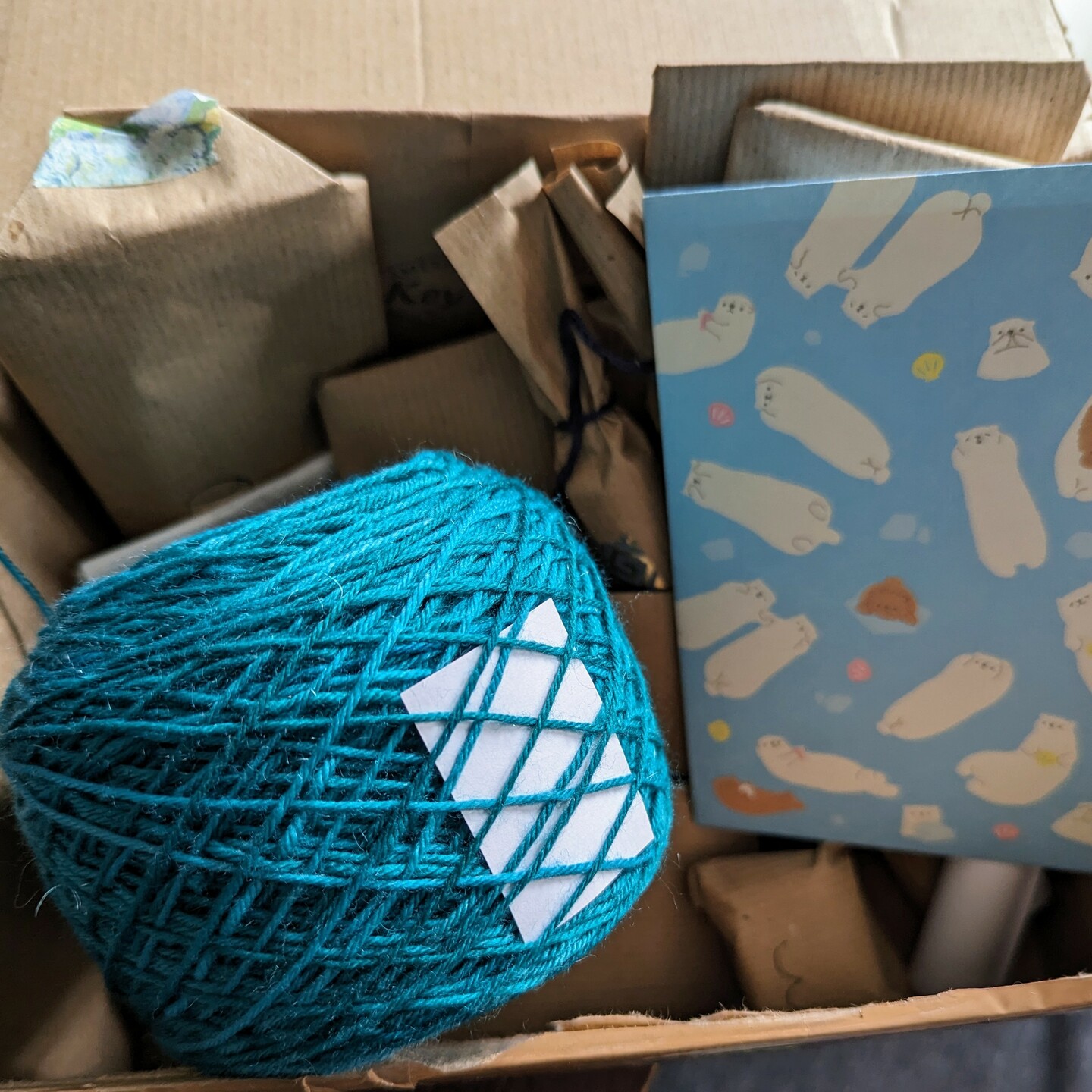 A ball of teal yarn with small paper notes on a pile of little gift packages in a box